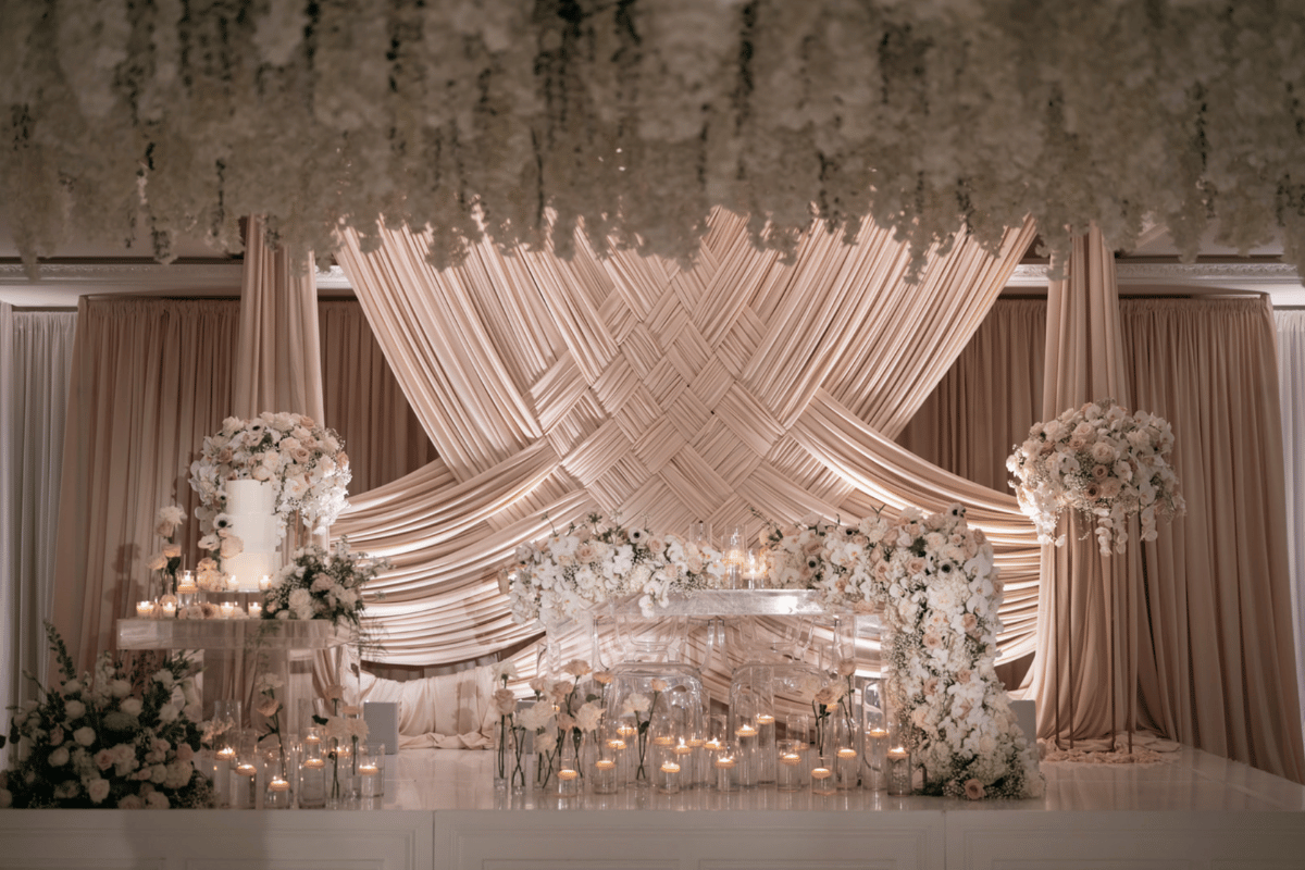 Luxurious wedding stage with criss-cross drape design, with white floral arrangements, and soft lighting from candles